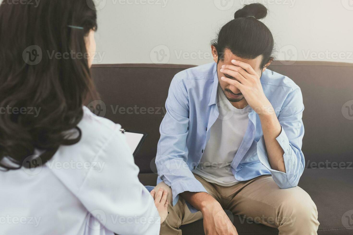 Asian young man, male suffers in mental need to therapy with psychologist while sitting on couch, consult with psychiatrist and encouragement patient by touching, holding to make his feel relaxed. photo