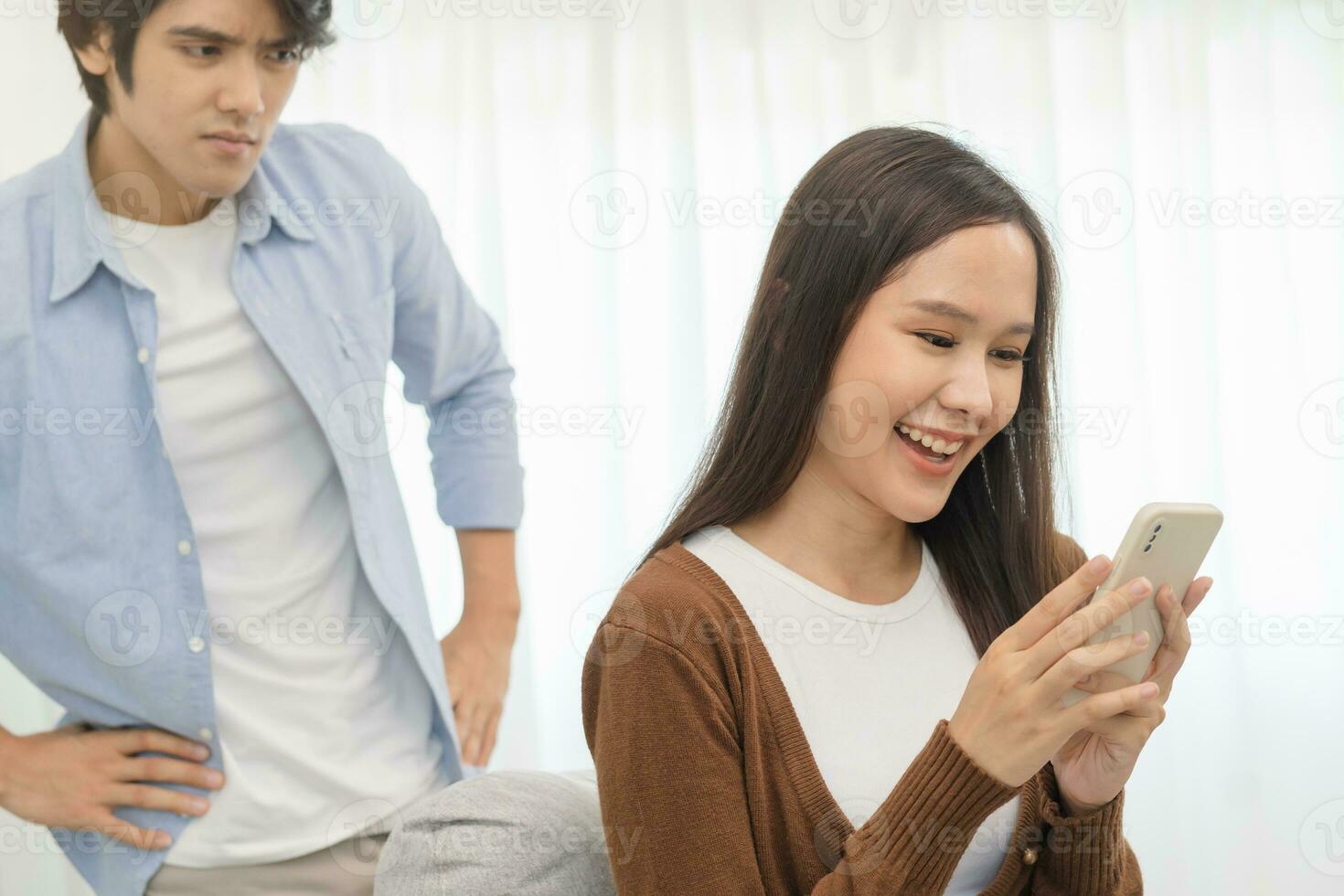Infidelity, suspicion asian young couple love, wife using mobile phone, husband watching spying his girlfriend while woman chat a message, man sneaky distrust and jealousy, relationship problem. photo