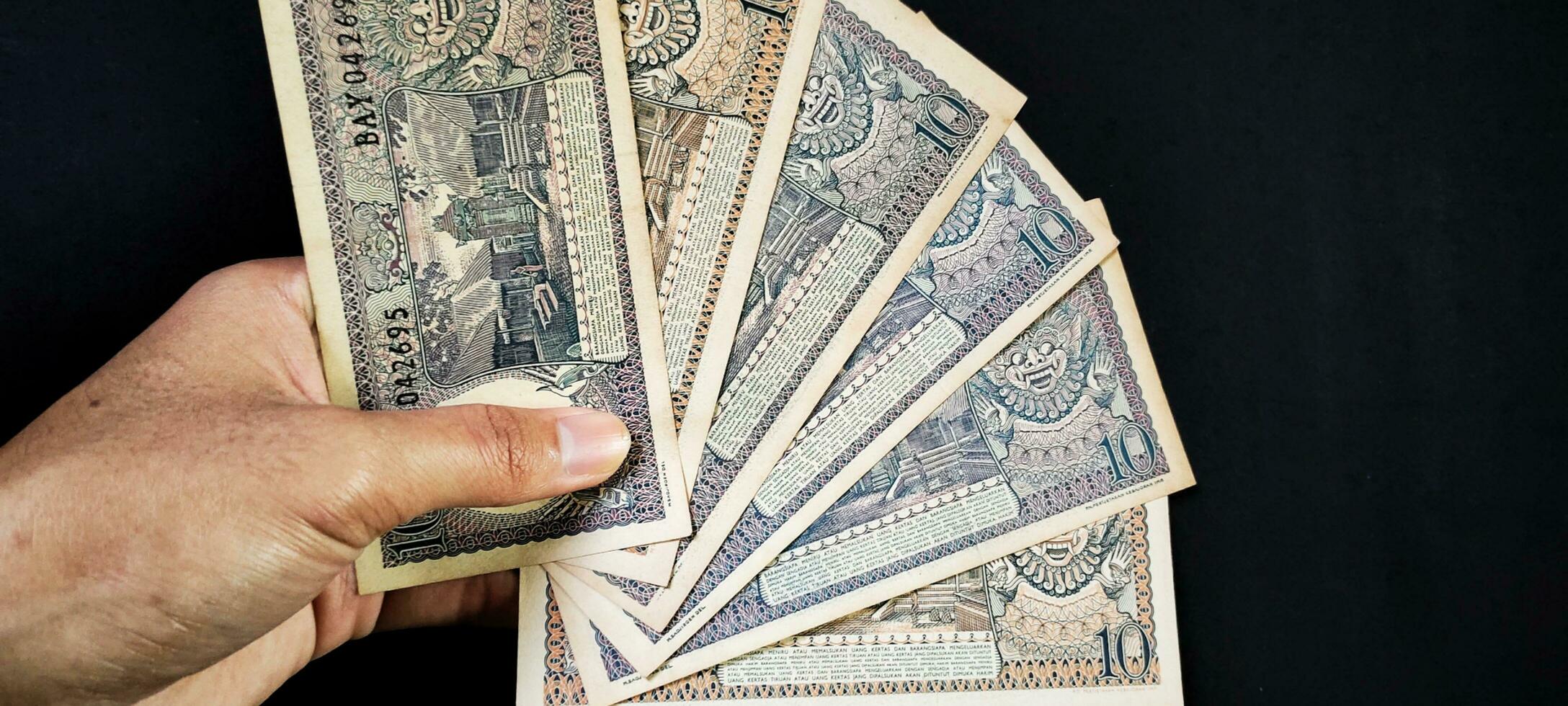 Man holding of old Indonesian banknotes Rp.10,00 issued in 1963. Old rupiah currency concept isolated on a black background. Top view photo