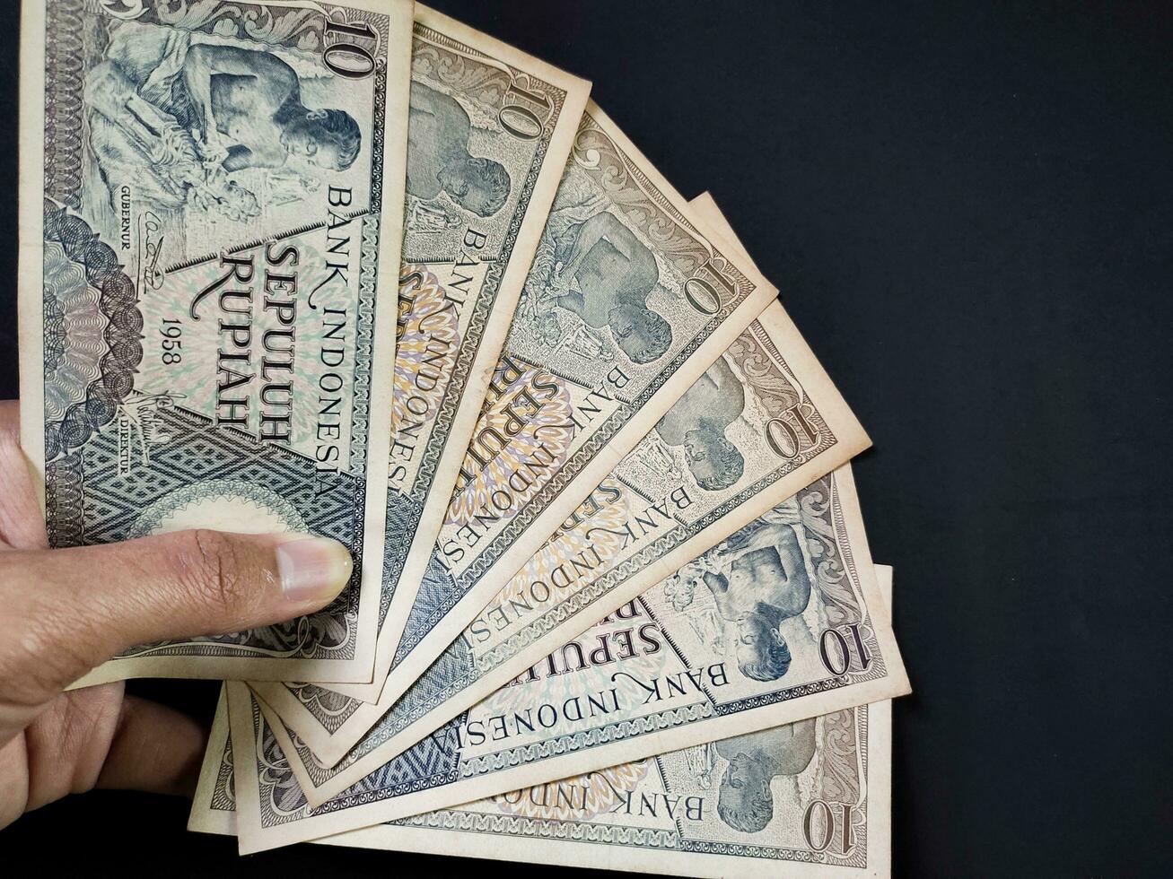 Man holding of old Indonesian banknotes Rp.10,00 issued in 1963. Old rupiah currency concept isolated on a black background. Top view photo