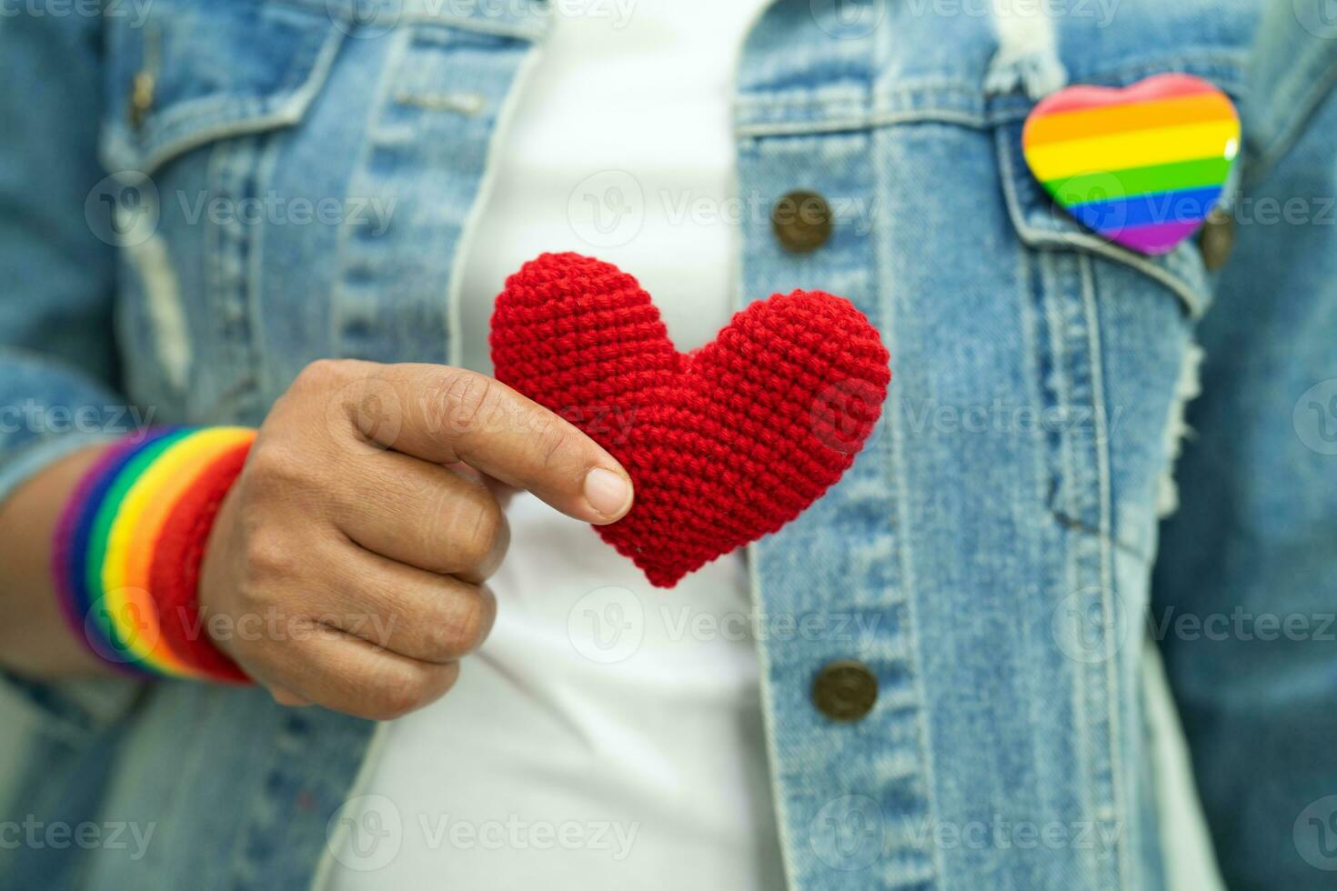 Asian lady wearing rainbow flag wristbands and hold red heart, symbol of LGBT pride month celebrate annual in June social of gay, lesbian, bisexual, transgender, human rights. photo