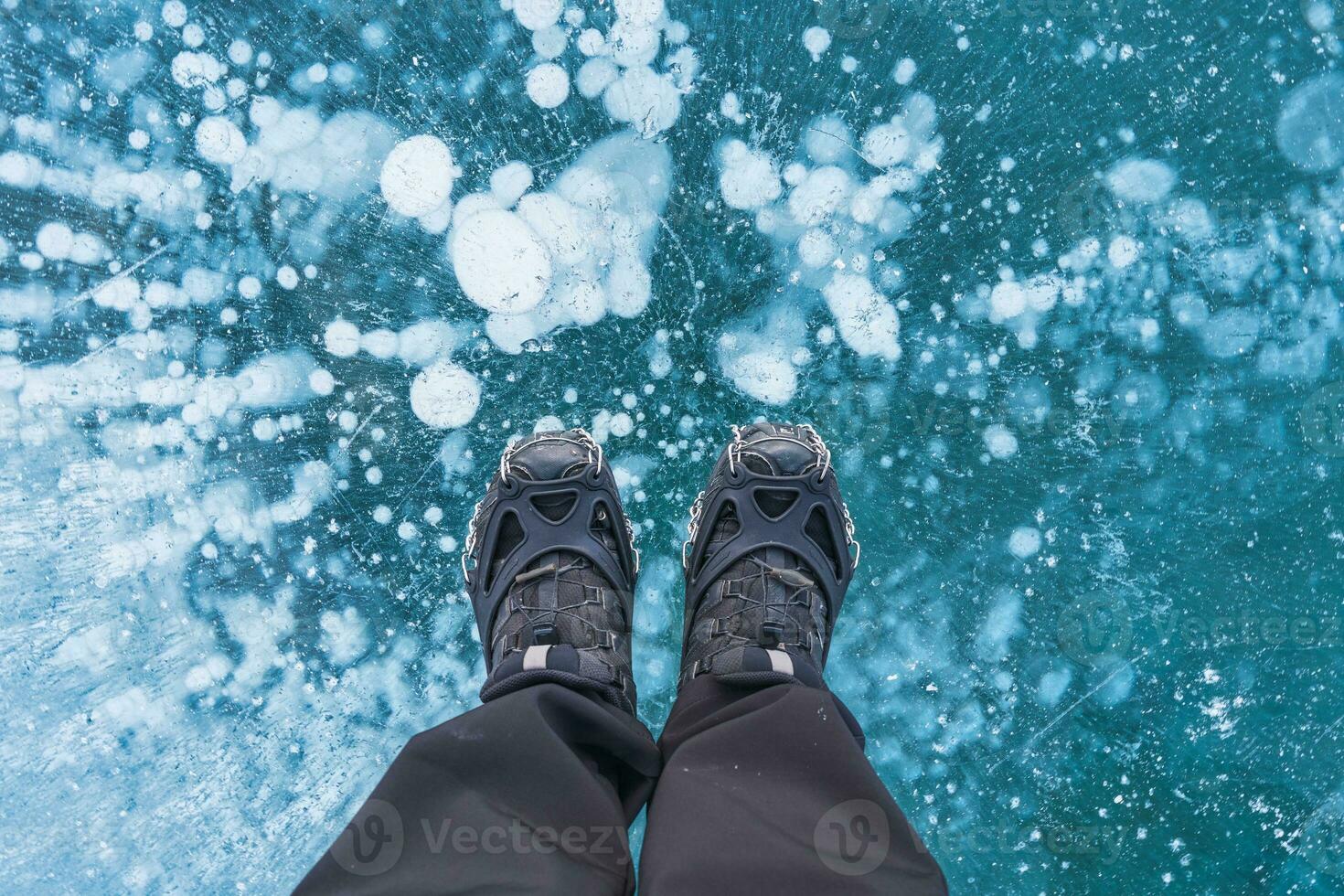 Man in boots standing on frozen lake with natural bubble in winter photo