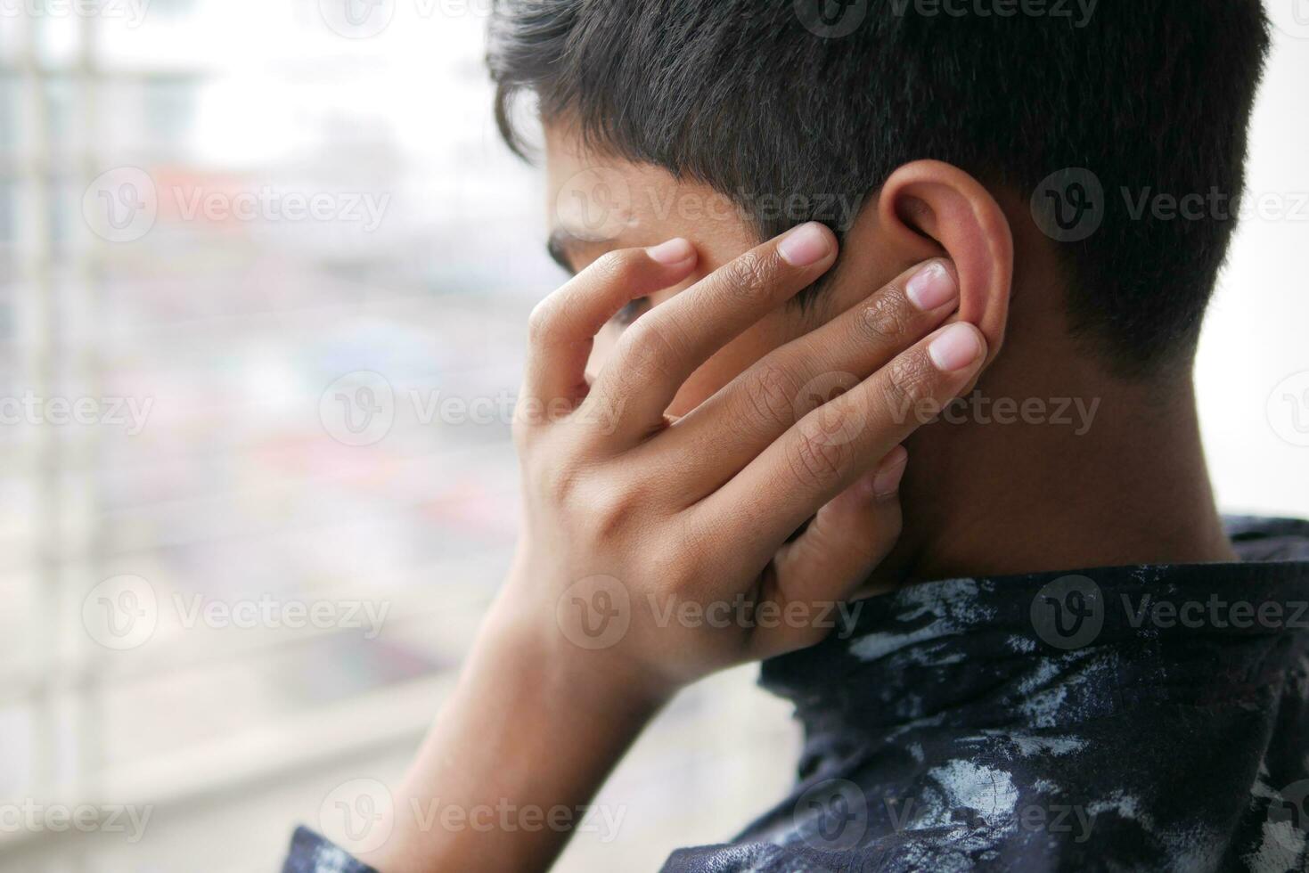 teenage boy having ear pain touching his painful ear , photo