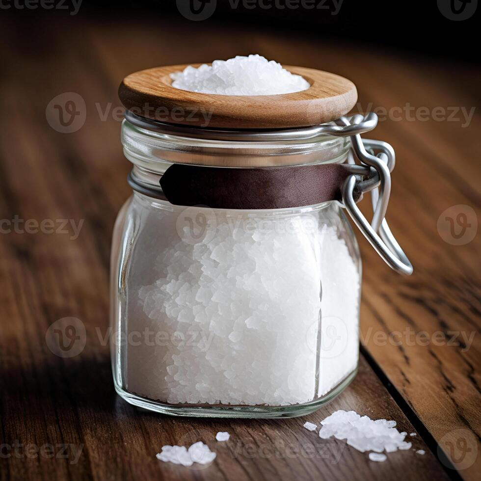 Rock salt in a glass jar with a wooden lid - a salt shaker on a wooden table. Blurred background, close-up. photo