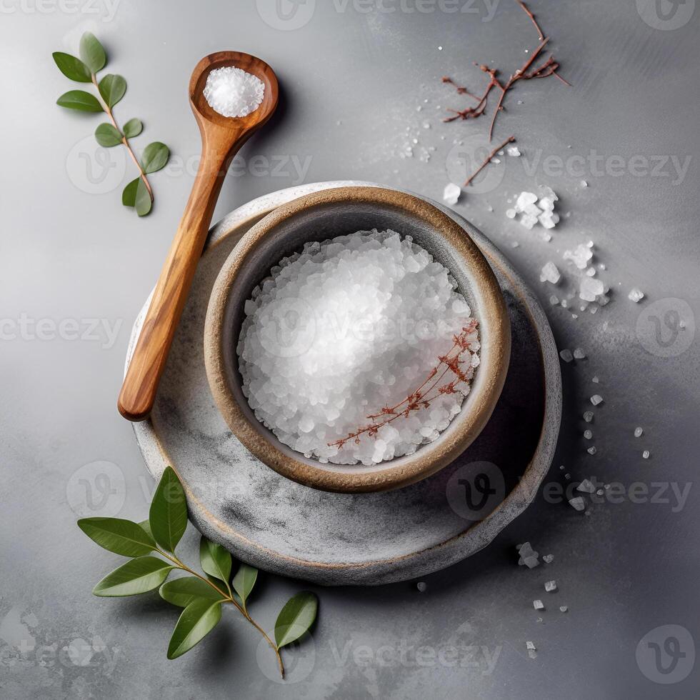 White salt is scattered on a marble table. Seasonings in earthenware, a wooden spoon on a gray background. . photo