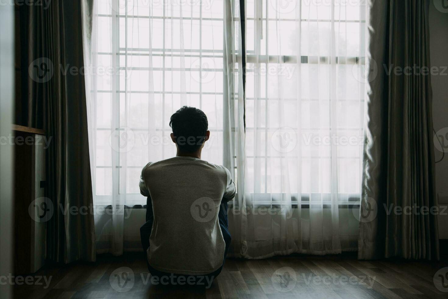 Alone man silhouette staring at the window closed with curtains in bedroom. Man stands at window alone photo