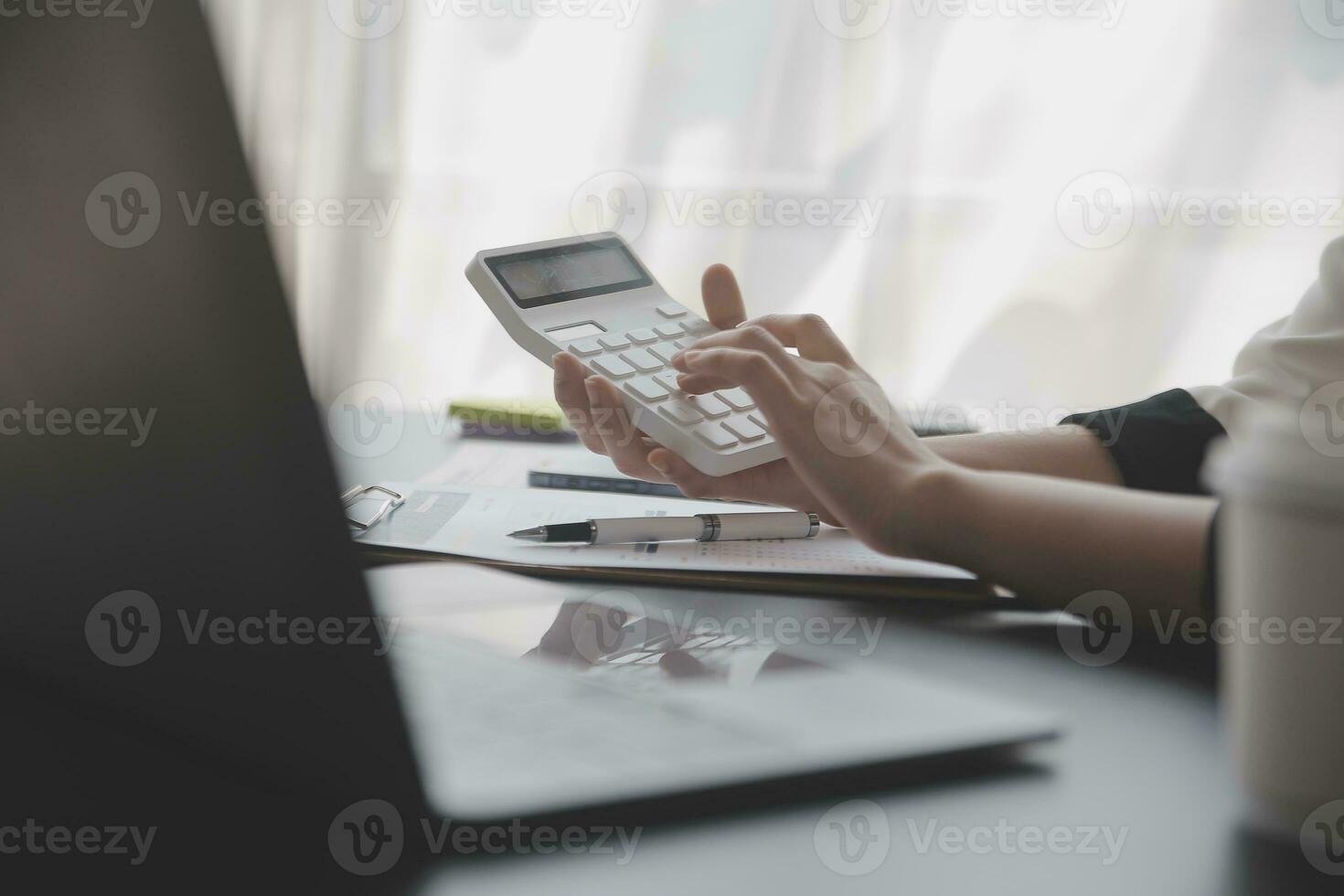 Asian Business woman using calculator and laptop for doing math finance on an office desk, tax, report, accounting, statistics, and analytical research concept photo