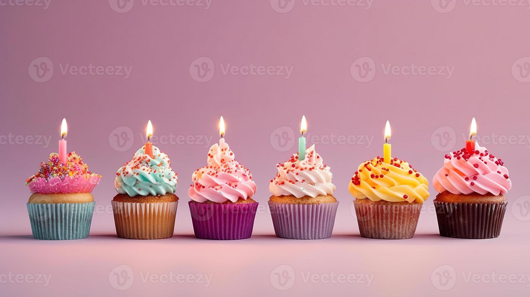 Row of colorful birthday cupcakes with candle of each, on light pink background. photo