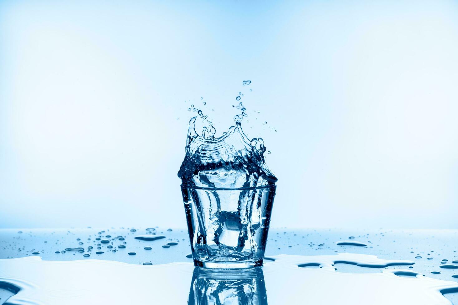 Ice that fell into the glass with water splashing from glass isolated on blue background photo