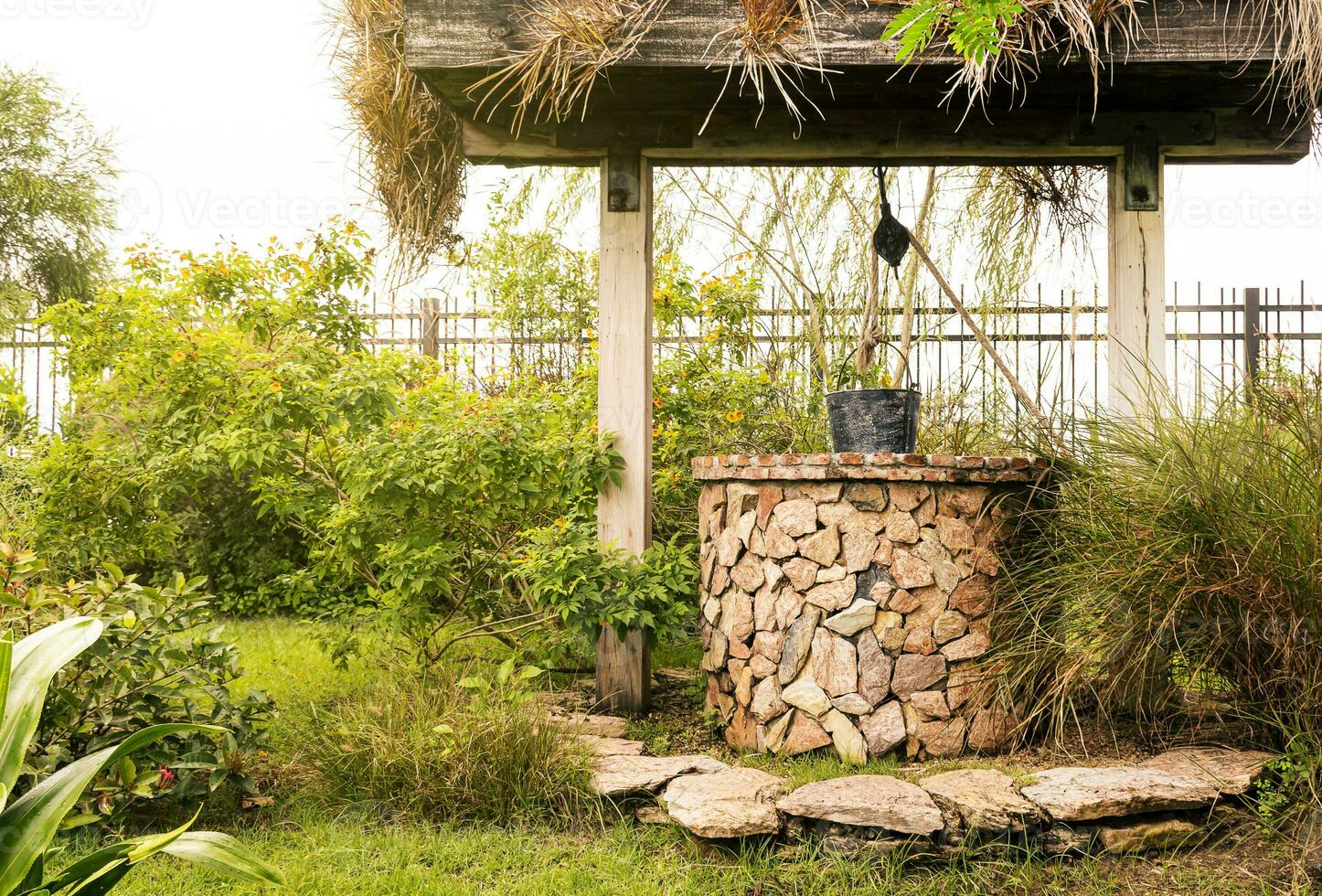 Vintage stone brick well with black steel bucket in garden photo