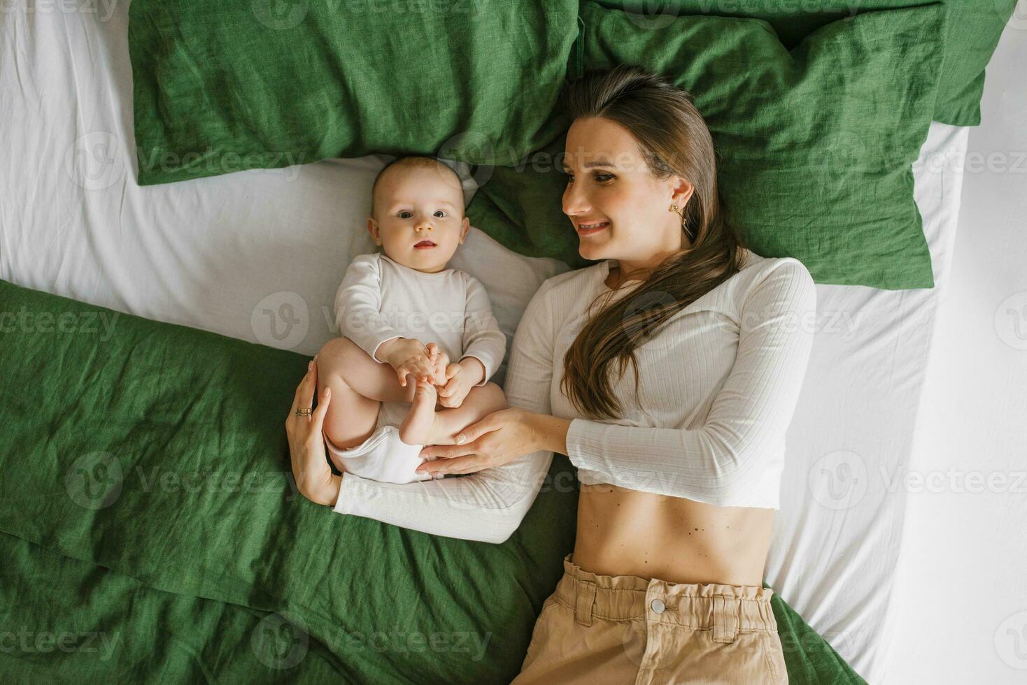 Happy smiling mother and child lying on the bed at home on the bed, top