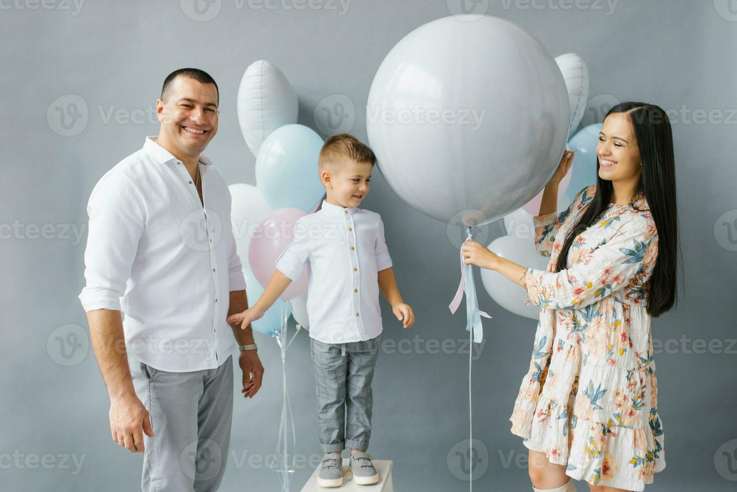 Gender reveal party. Stylish beautiful family with a baby pop a balloon to find out the gender of the unborn child in the family photo
