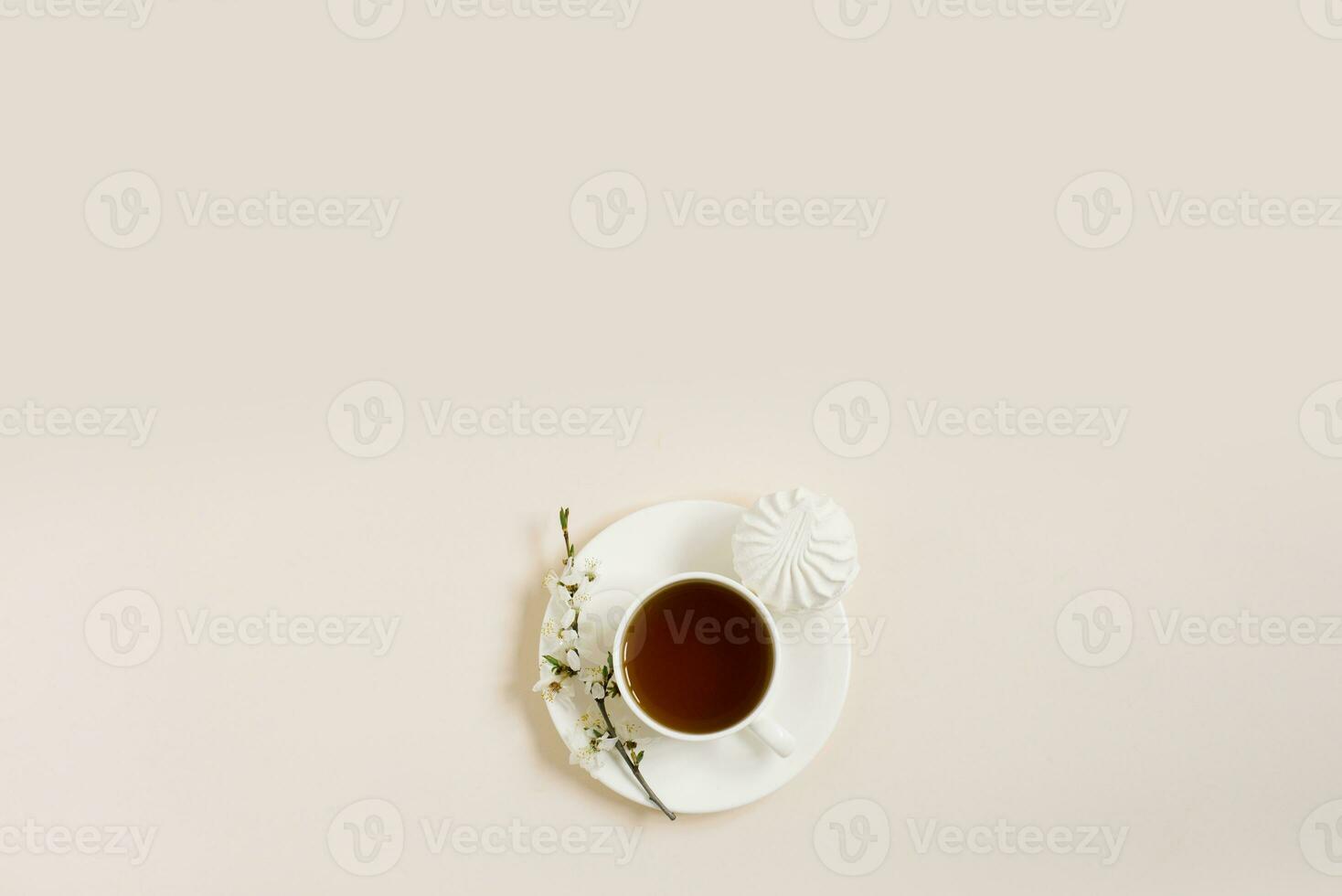 Spring concept. Cup of morning black tea with sweets marshmallows on beige background with sprig of blooming apple tree with copy space photo