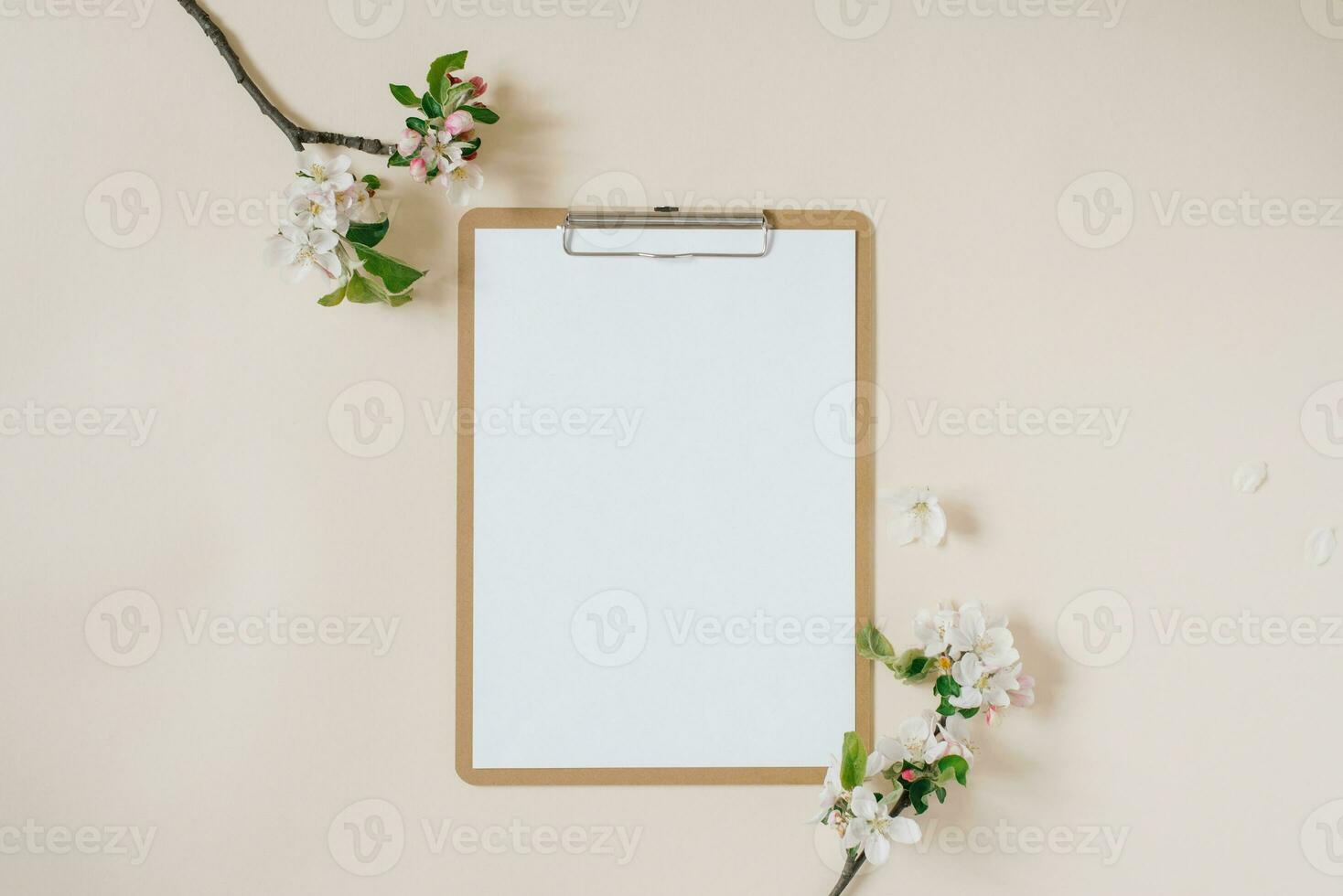 Clipboard tablet pad with blank copy space and white apple flowers on beige backdrop. Flat lay, top view template. Female office desk photo
