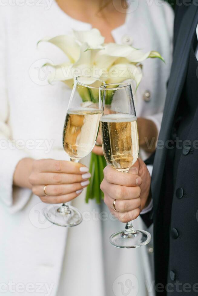 The bride and groom are holding two champagne glasses for the wedding ceremony photo