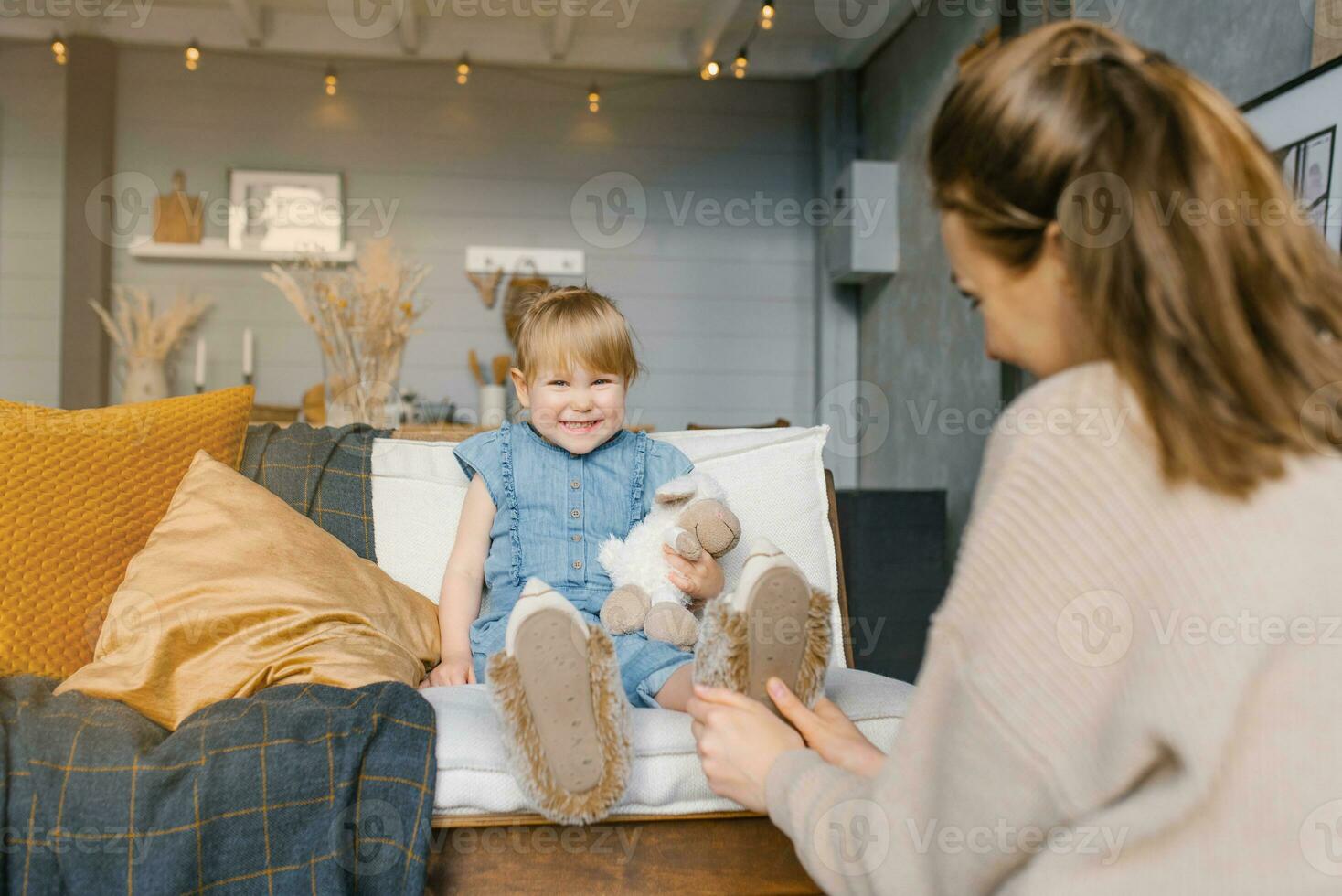 Mom puts on her daughter's slippers while sitting on the couch in the house photo