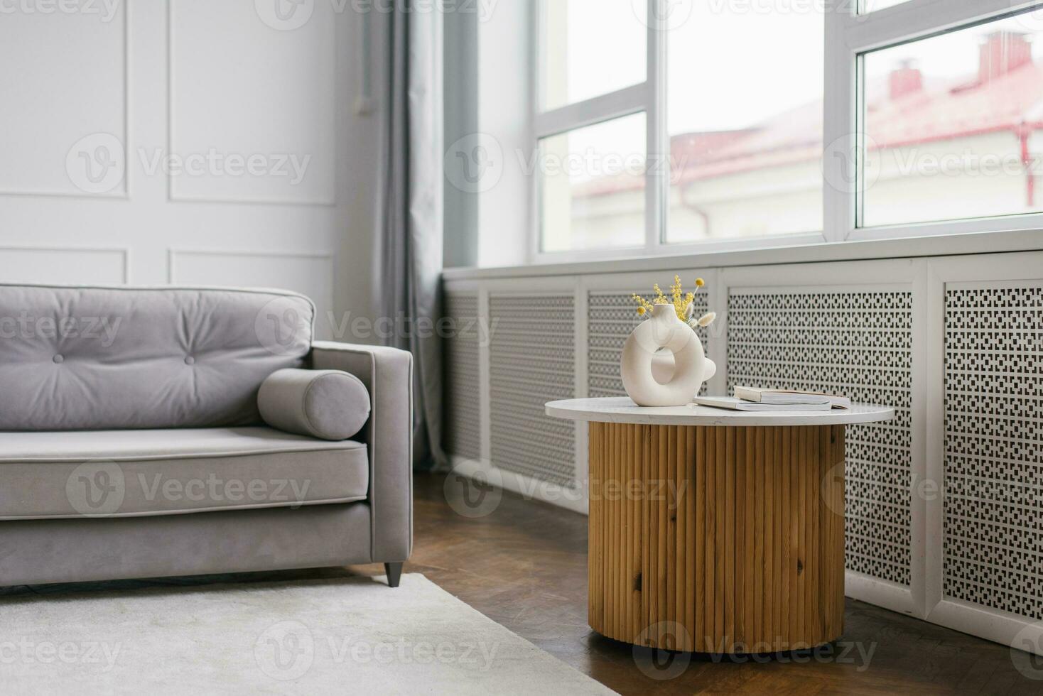 interior de un moderno vivo habitación con un gris sofá y un café mesa cerca el ventana con un florero con mimosa foto