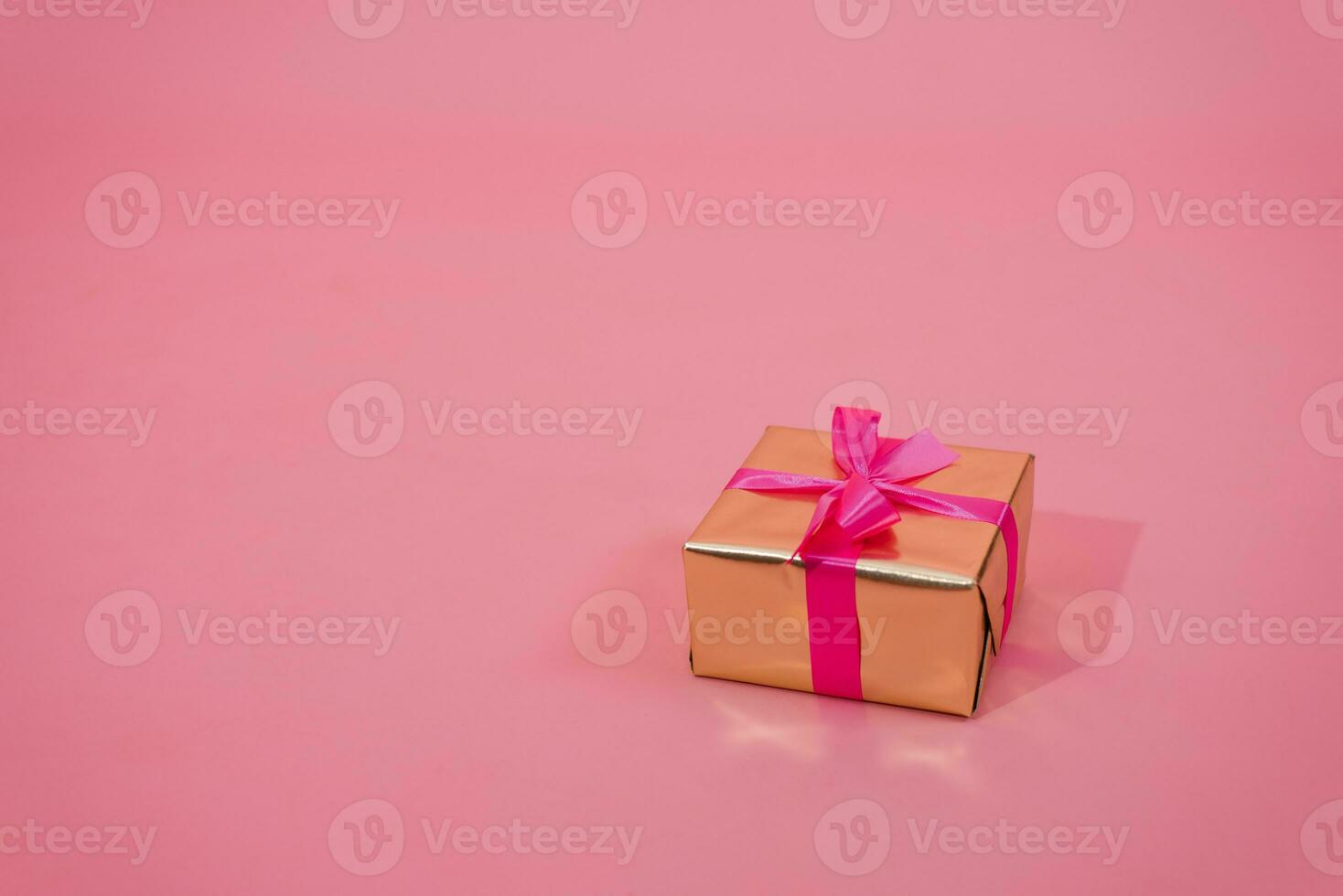 Gift box in gold paper decorated with fuchsia bow on pink background with copy space photo