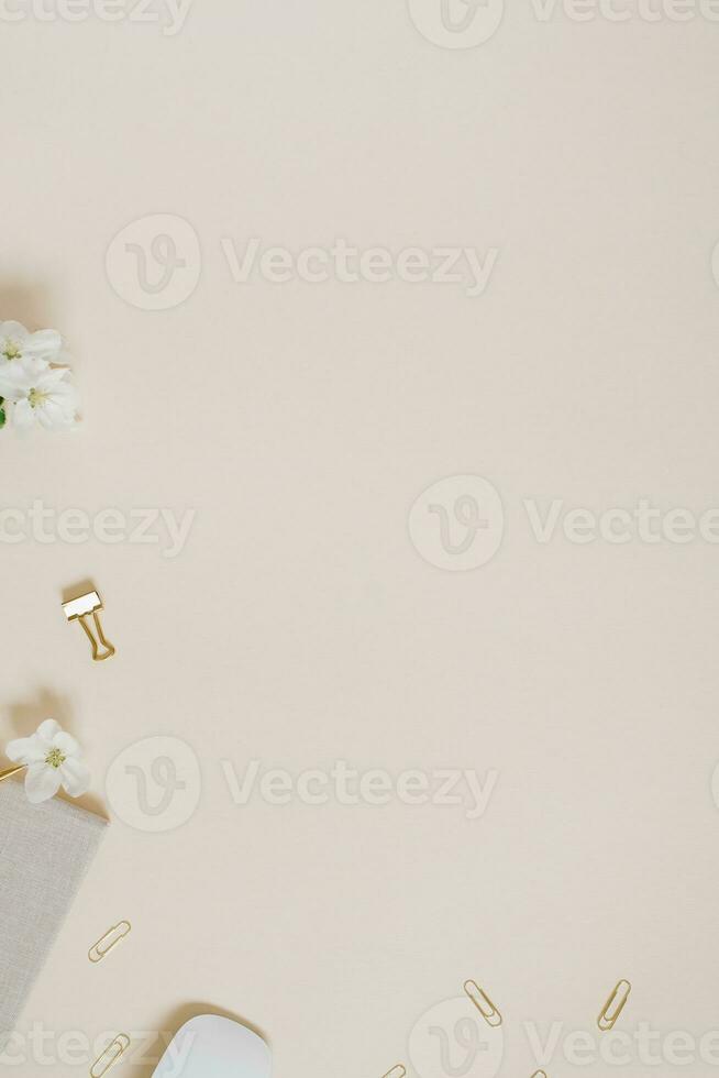 Female workspace of a table with delicate flowers of an apple tree, a notebook, a pen, paper clips and a mouse on a delicate beige background. flat lay, top view photo