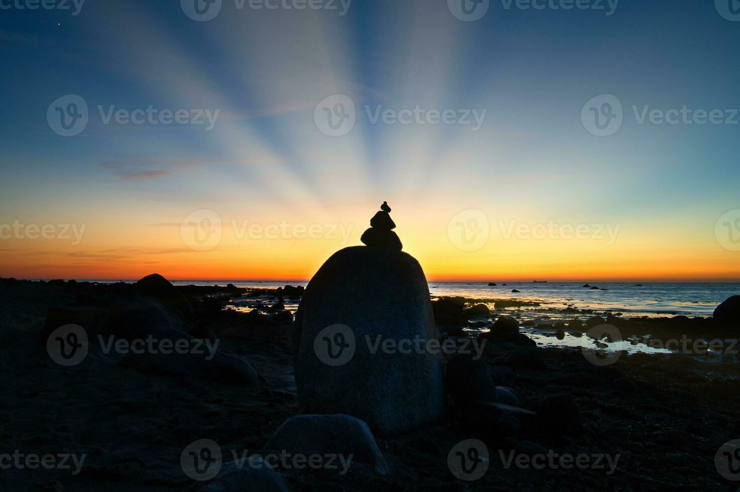 Stone pyramid on the Baltic Sea overlooking the sea at sunset. Sun shines behind stone photo