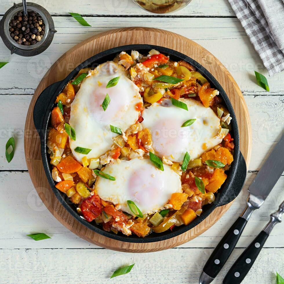 Shakshouka in frying pan. Fried eggs with vegetables, tomato, pepper, pumpkin and onion. Top view photo