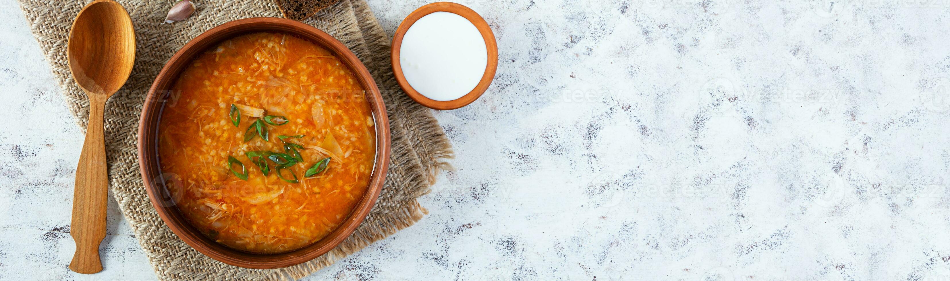 Cabbage soup in bowl with green onion, bread and salo on white background. Top view photo