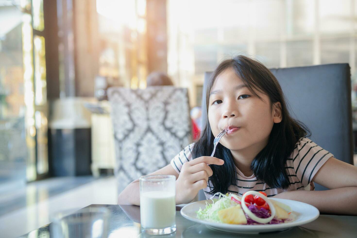 asiático linda pequeño niña comiendo Fresco tomate y ensalada en Mañana. foto