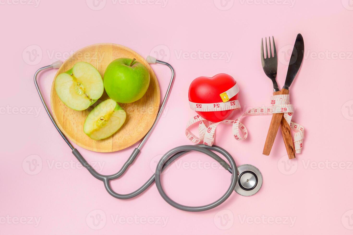 Green apple on dish with stethoscope and measuring tape around fork and knife photo