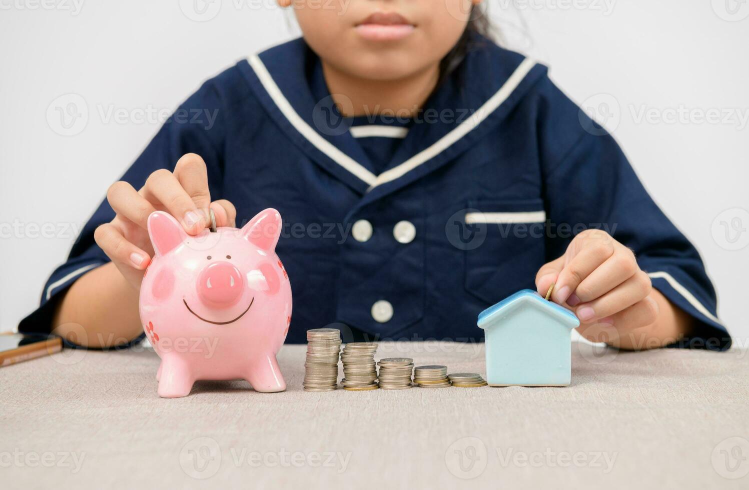 asian girl putting coins to piggy bank and little house on white background photo