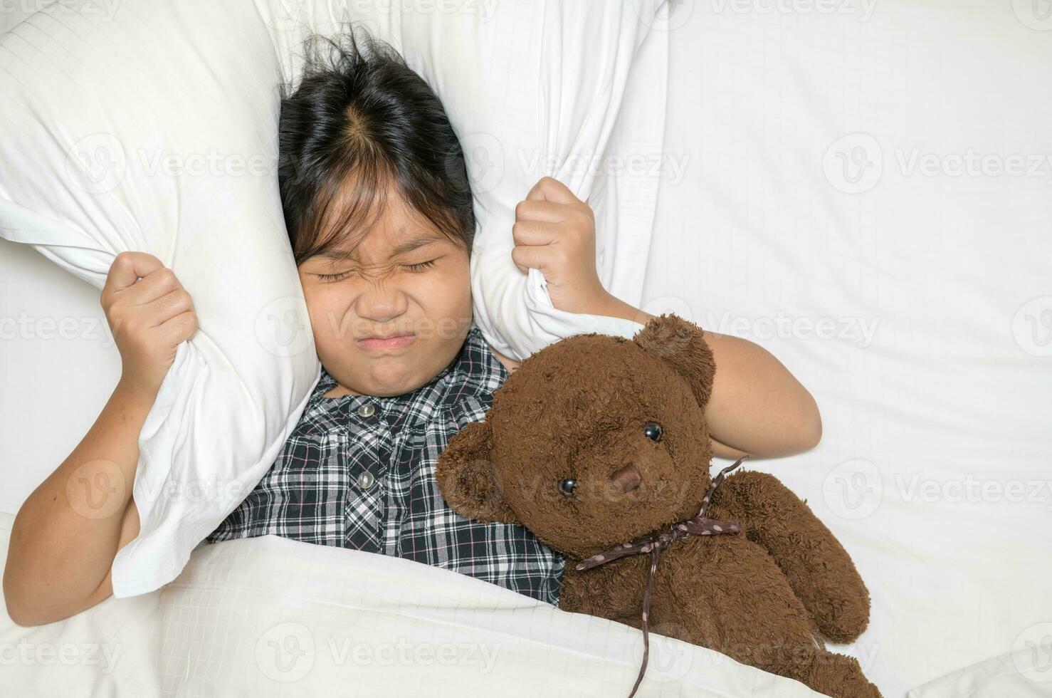 Little girl lying in bed covering head with pillow because too loud