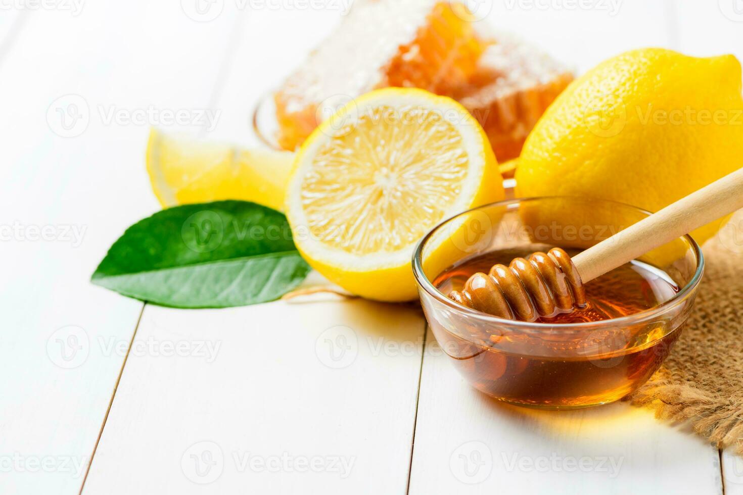 Honeycomb on dish with honey dipper with lemons on white wood background, photo