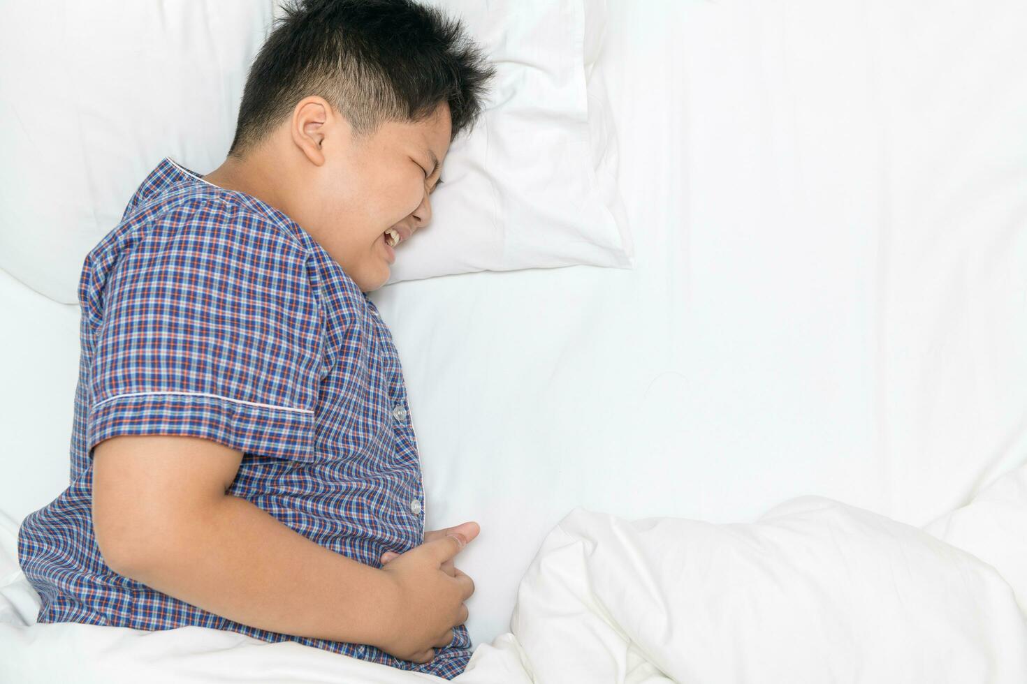 asian child suffering from stomachache and lying on bed top view s photo