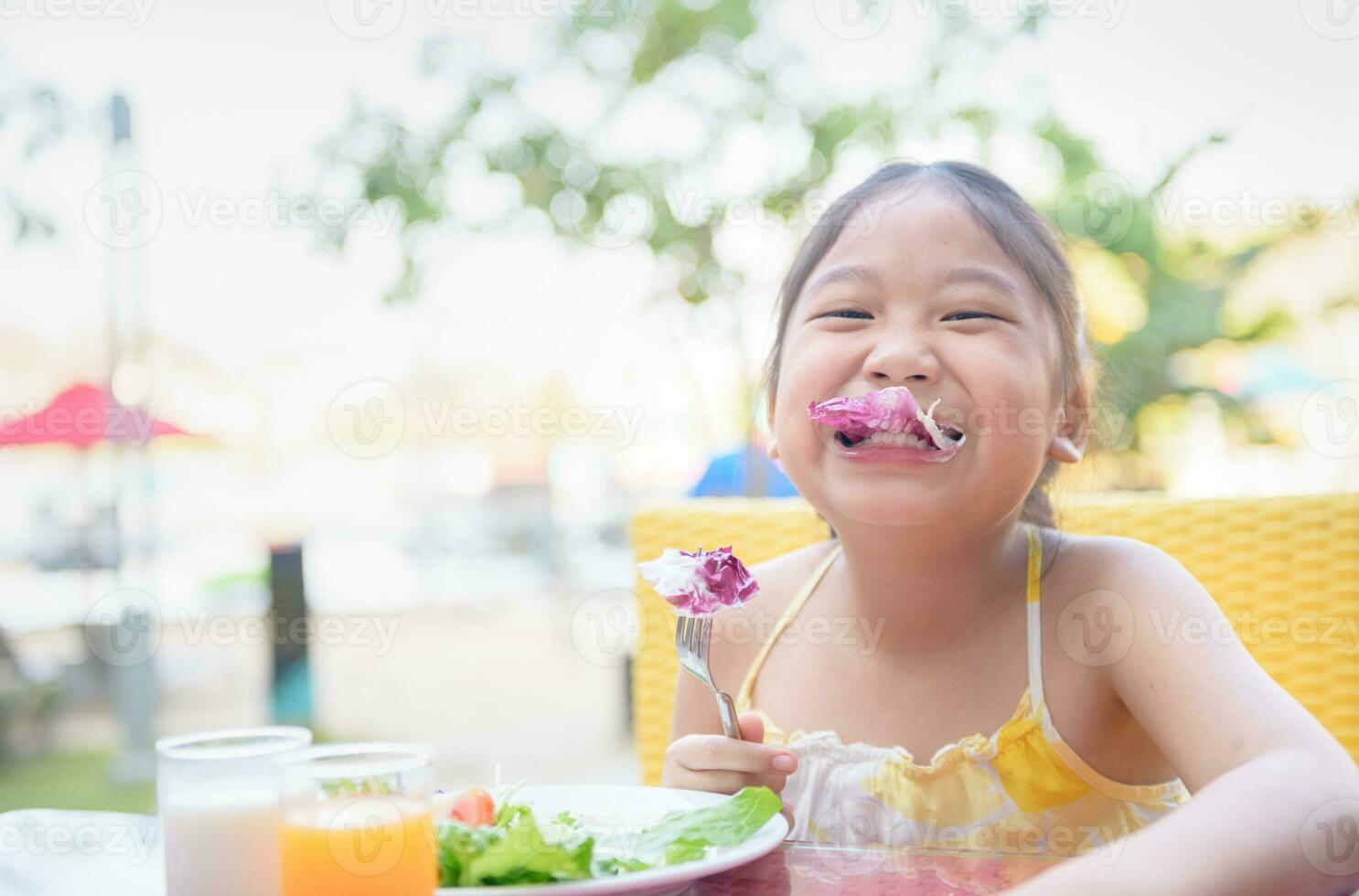 linda pequeño niña comiendo Fresco vegetales y ensalada en Mañana. foto