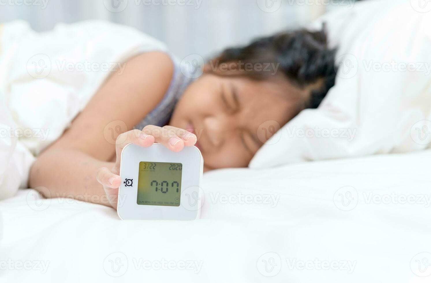 Hand girl reaching out for alarm clock on morning, photo