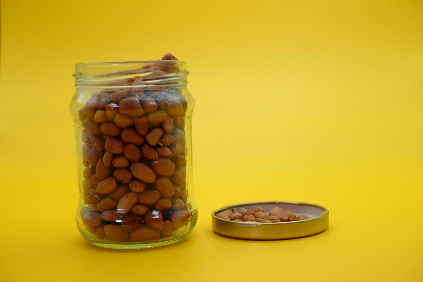 open glass jar filled to the brim with shelled nuts. glass bottle filled with peanuts isolated on yellow background. photo