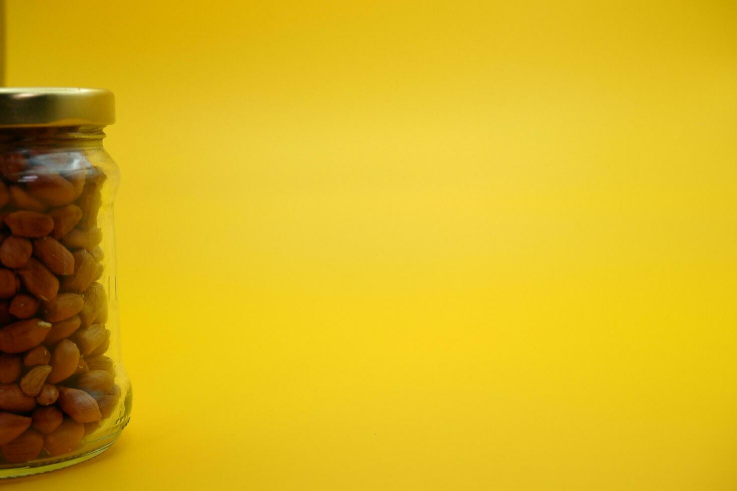 glass jar filled to the brim with shelled nuts. glass bottle filled with peanuts isolated on yellow background. photo
