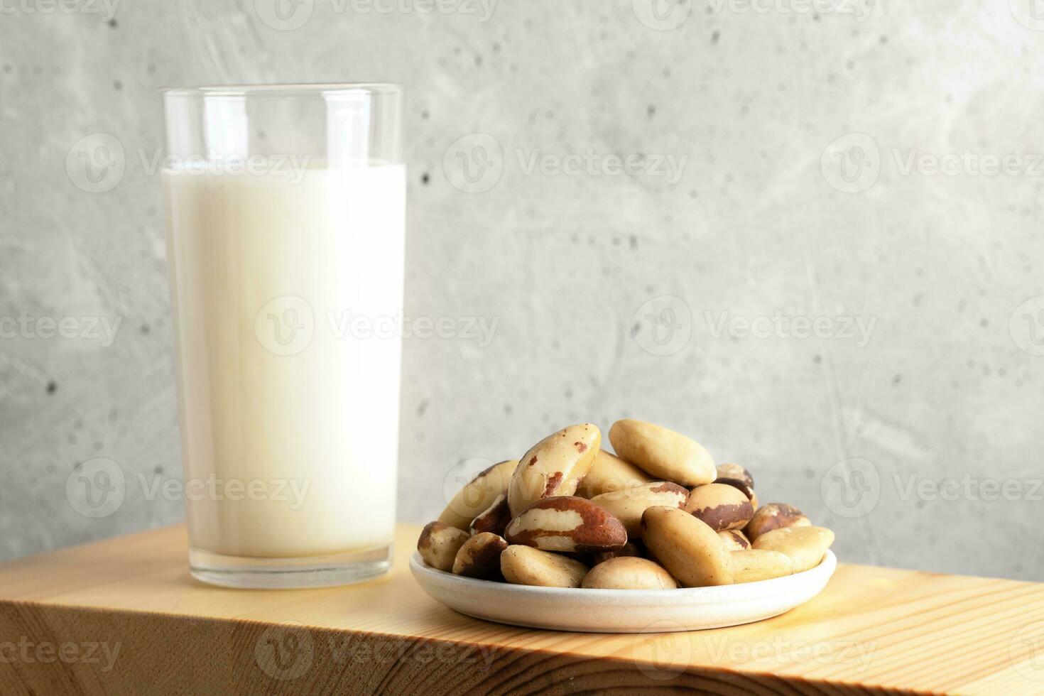 One glass of vegan milk made of brazil nut and nuts in plate on wooden board. Close up. Copy space. photo