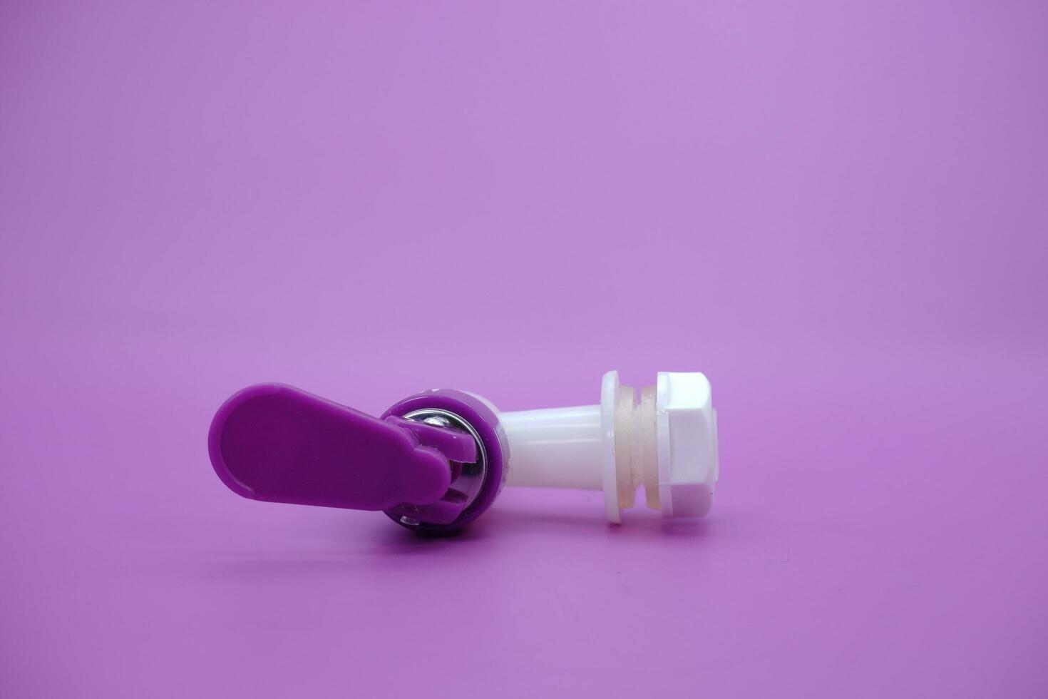 closed faucet isolated purple background. the faucet is white with a purple lid photo