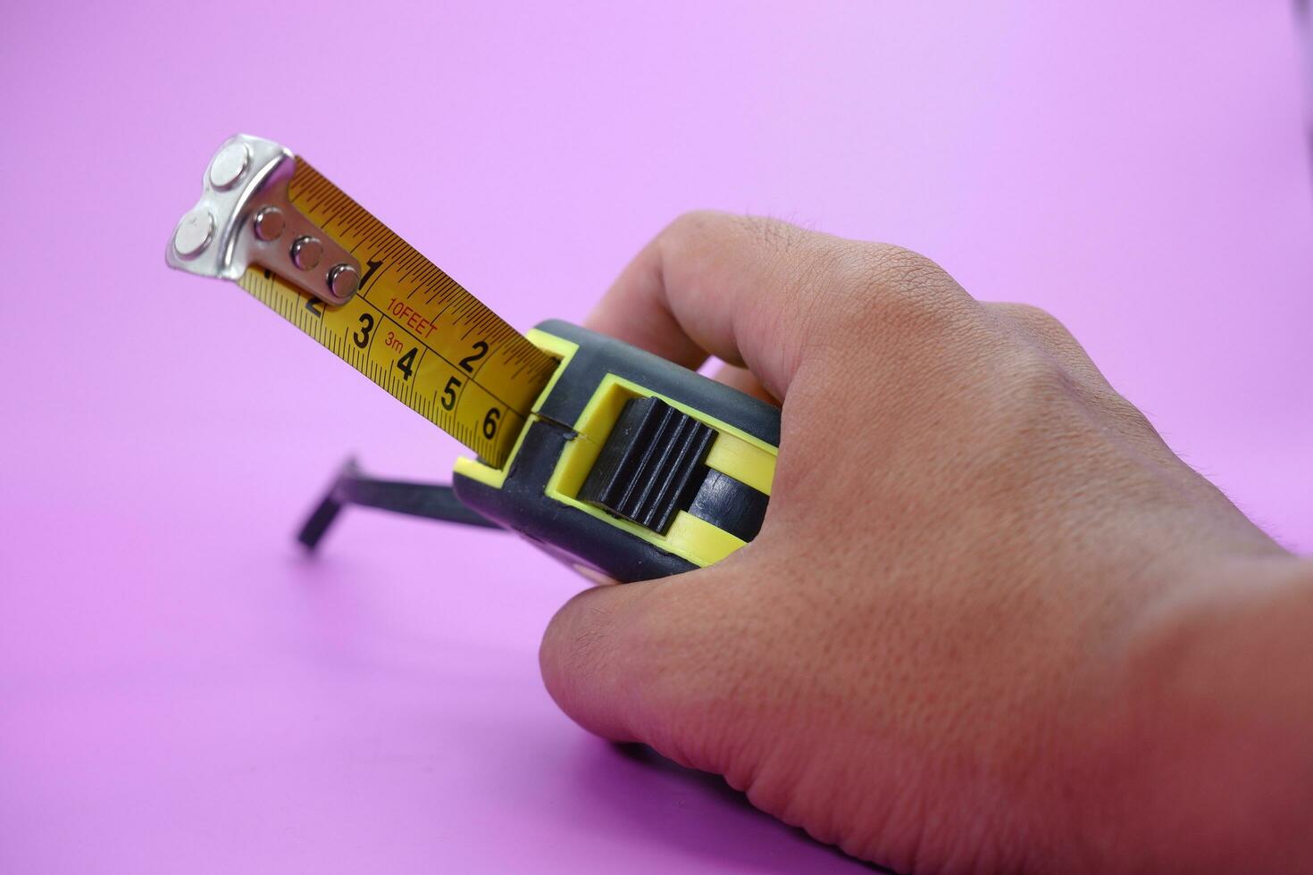 https://static.vecteezy.com/system/resources/previews/025/287/563/non_2x/hand-holding-tape-measure-isolated-purple-background-measuring-tool-used-by-builders-free-photo.JPG