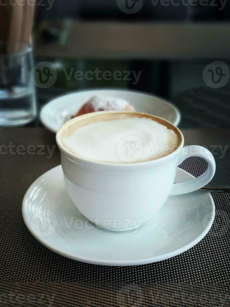 alto ángulo ver un taza de latté, moca o capuchino café en el blanco taza en desayuno mesa con oscuro antecedentes foto