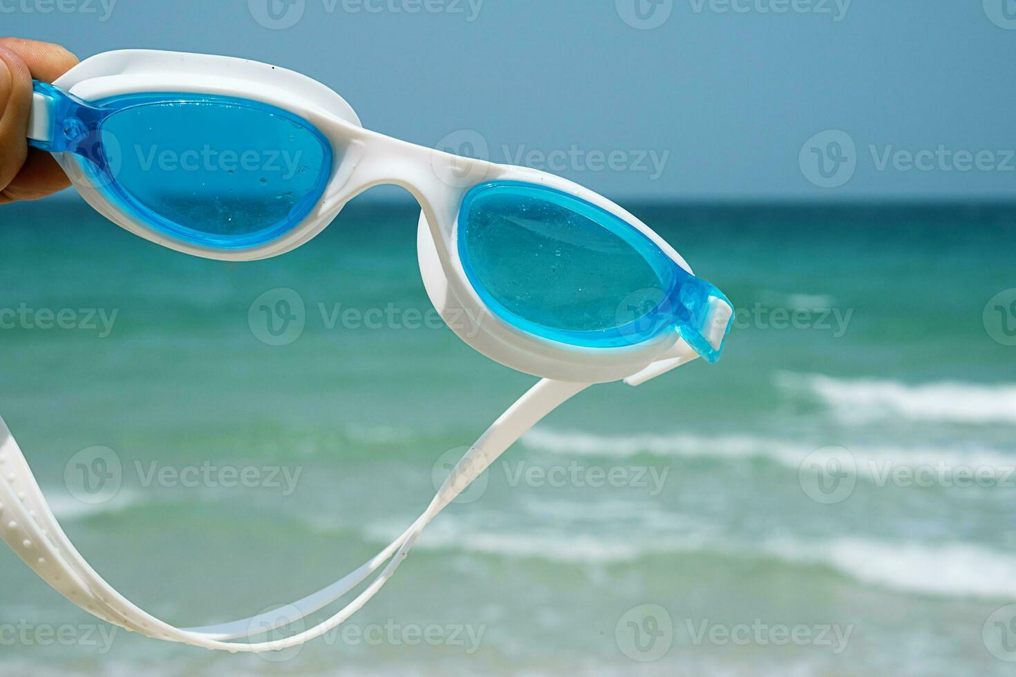 Hand holds swimming goggles agaist seascape. Tropical vacation concept. photo