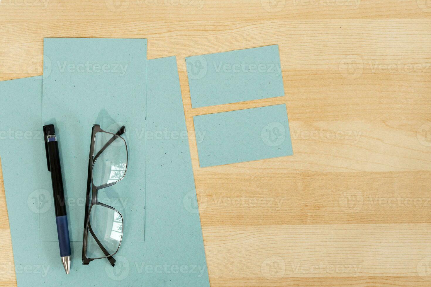 Top view of office work space, wooden desk table with eyeglasses, blue textured paper and business card. photo