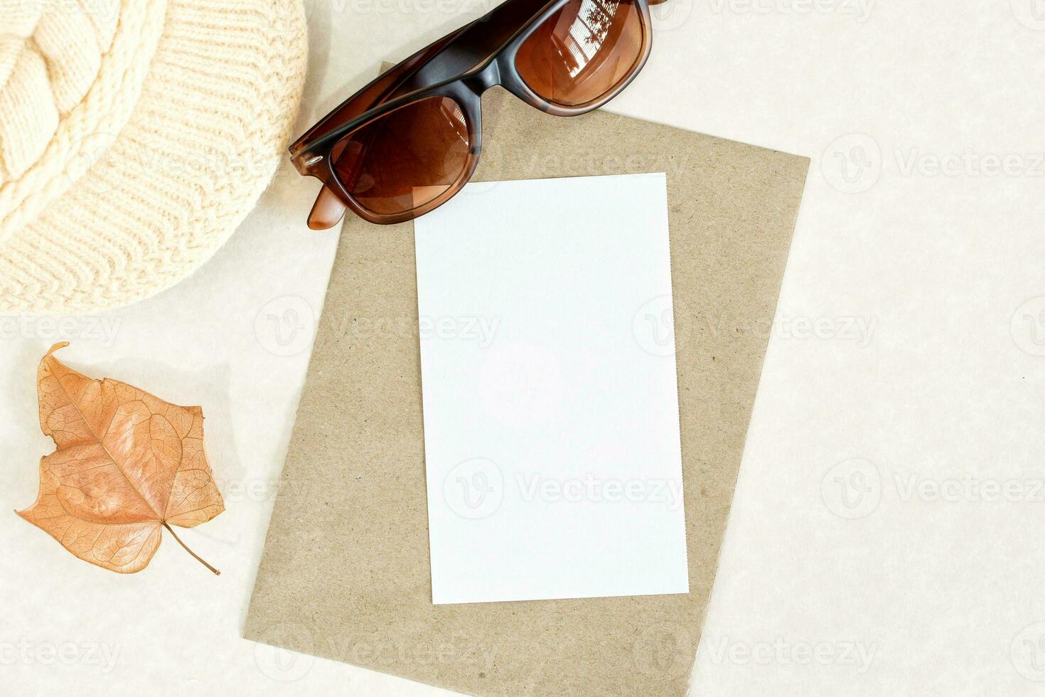 Invitation or greeting card mockup with dry leaf, sunglasses and woolen cap decorations. photo