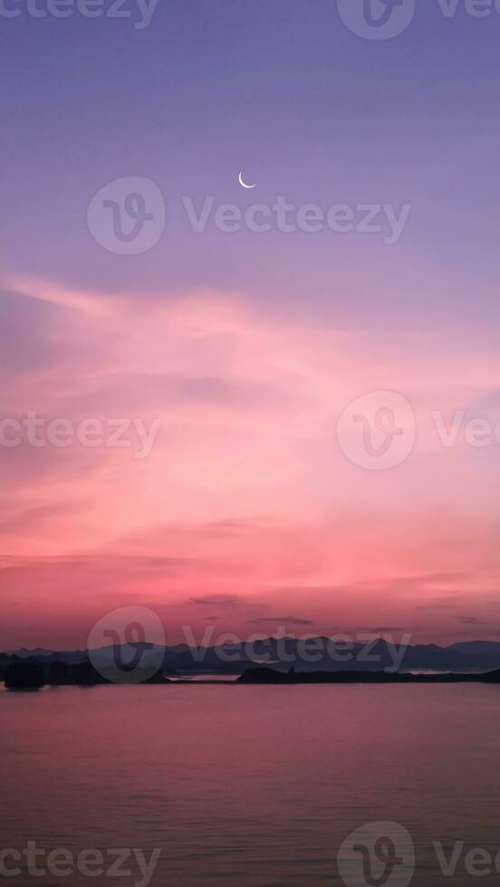 Vertical image, crescent moon in dramatic vibrant color sky with silhouette landscape of mountains and lake, twilight, nature wallpaper background photo