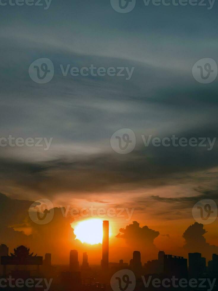 vertical imagen, puesta de sol en el noche con dramático forma y color de nubes y cielo con silueta de paisaje urbano, edificio horizonte, naturaleza antecedentes foto