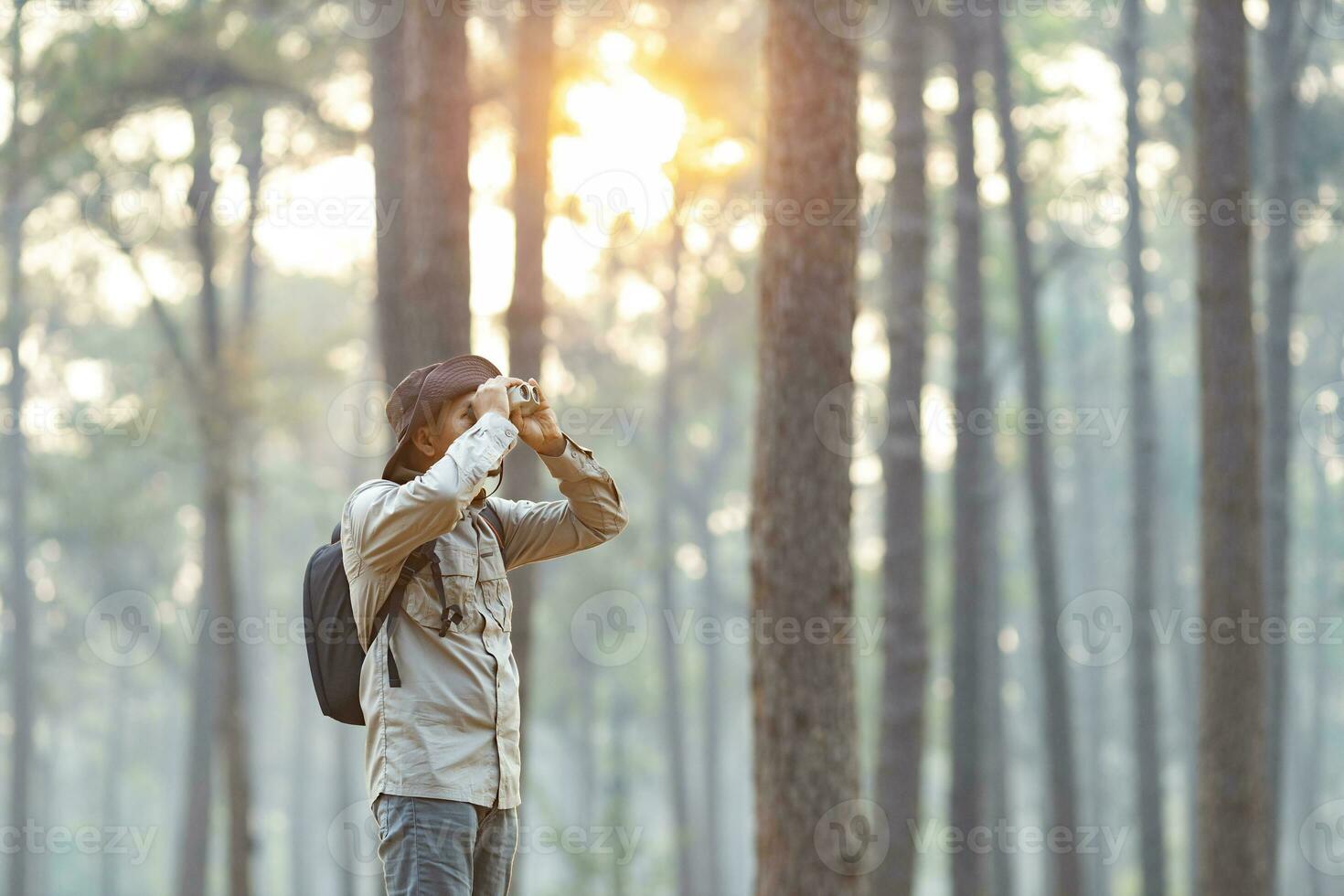 Bird watcher is looking through binoculars while exploring in the pine forest for surveying and discovering the rare biological diversity and ecologist on the field study concept photo