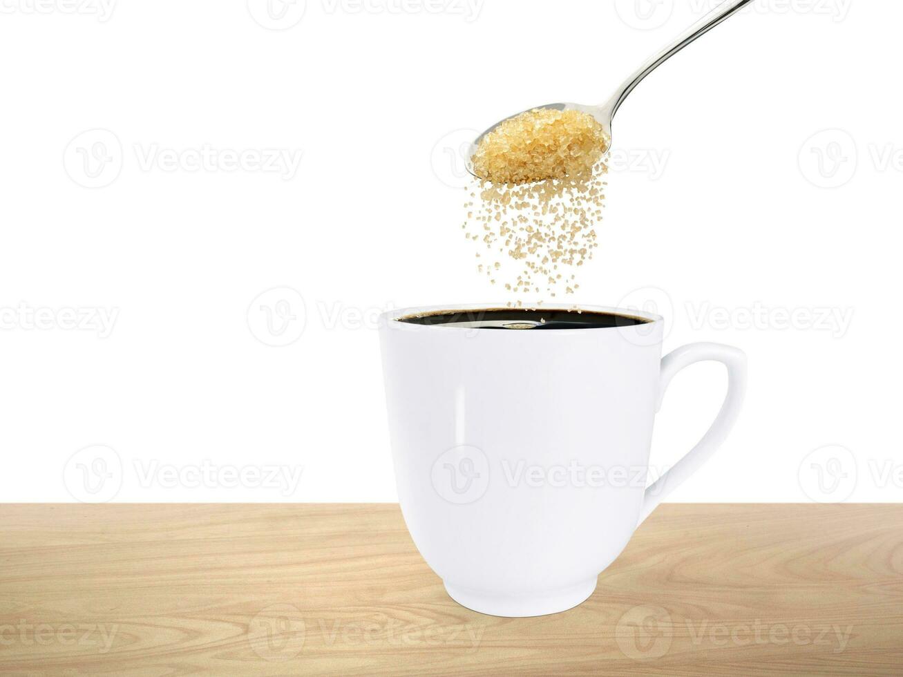 A spoonful of granulated sugar is poured into a white coffee mug placed on a wooden floor. photo