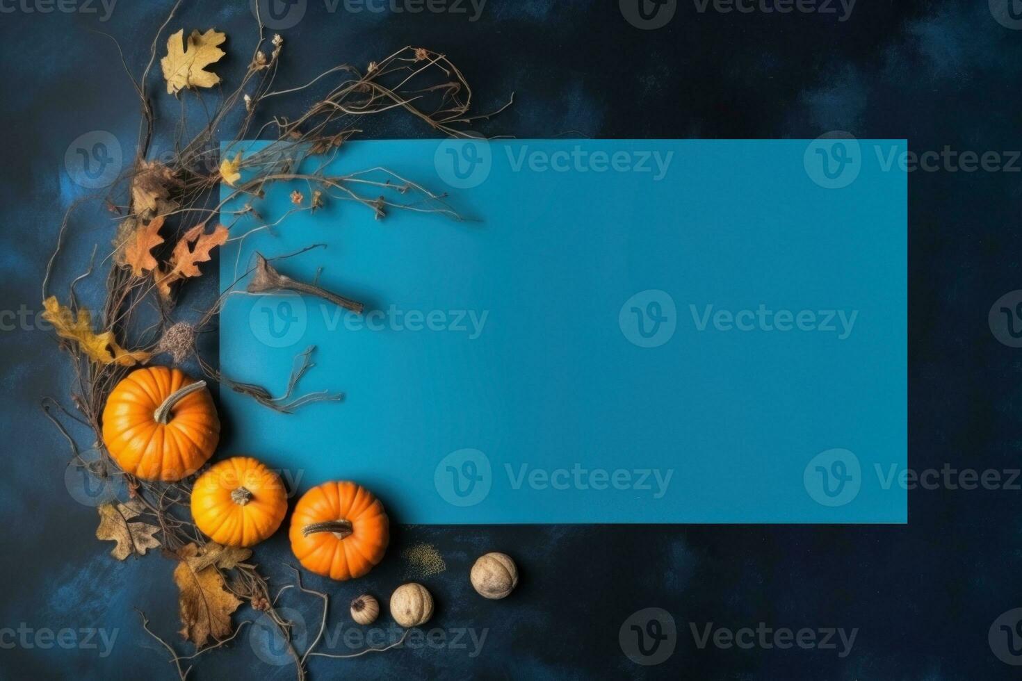 Light blue blank rectangular sheet and pumpkins, leaves, twig on dark blue textured background. photo