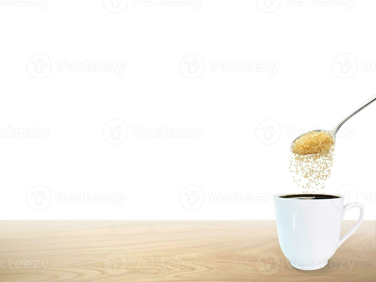A spoonful of granulated sugar is poured into a white coffee mug placed on a wooden floor. photo