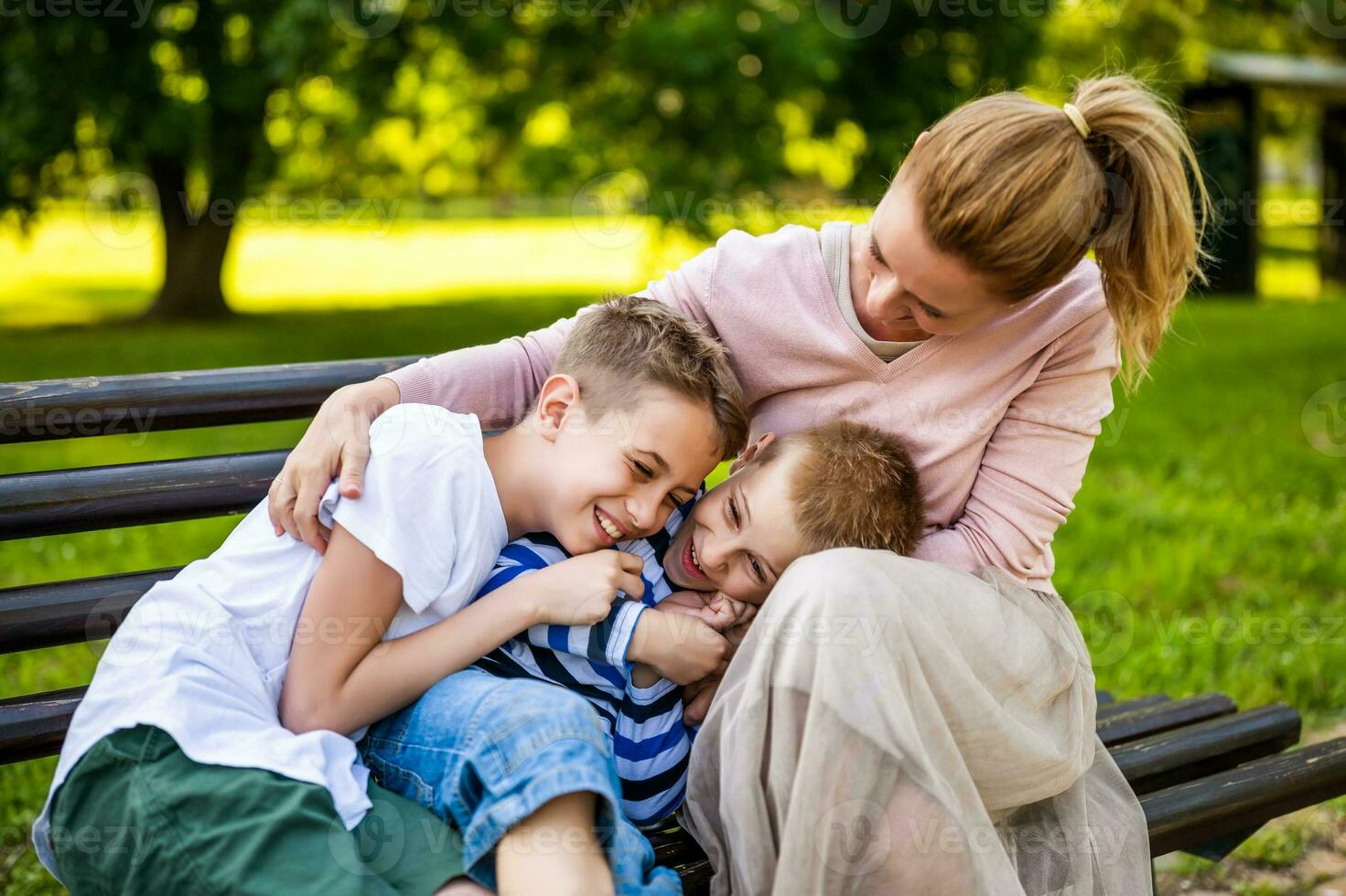 Happy mother is sitting with her sons on bench in park. They are having fun together. photo